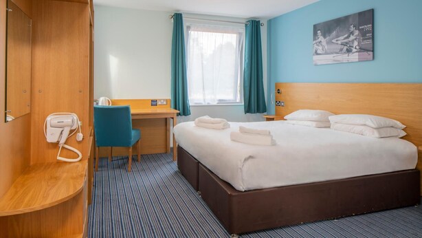 Habitación de hotel con cama, escritorio, silla, teléfono y ventana con cortinas.