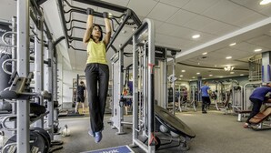 Un gimnasio con diversos equipos de ejercicio, incluyendo una barra de dominadas, máquinas de pesas y una plataforma elevada.
