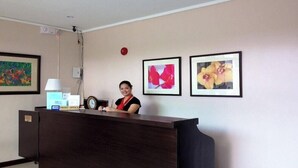 A reception desk with a clock, framed artwork, and a desk lamp. - Oftana Suites (Mandaue)
