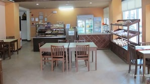 A restaurant interior with a counter displaying baked goods, a seating area with tables and chairs, and a display case with pastries. - Oftana Suites (Mandaue)