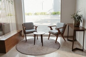 A modern room with two grey armchairs, a small round table, a wooden side table, and a potted plant. - Eco Express Hotel Poliforum (León)