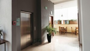 A modern hotel lobby with a reception desk, a plant, a dining area with chairs, and an elevator. - Eco Express Hotel Poliforum (León)