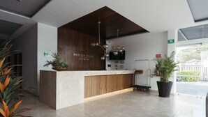 A hotel reception desk with a wooden finish, a modern chandelier, and potted plants. - Eco Express Hotel Poliforum (León)