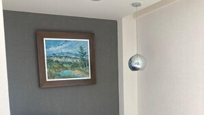 A modern living room with a grey sofa, a framed landscape painting, a glass coffee table, and a ceiling-mounted light fixture. - Eco Express Hotel Poliforum (León)