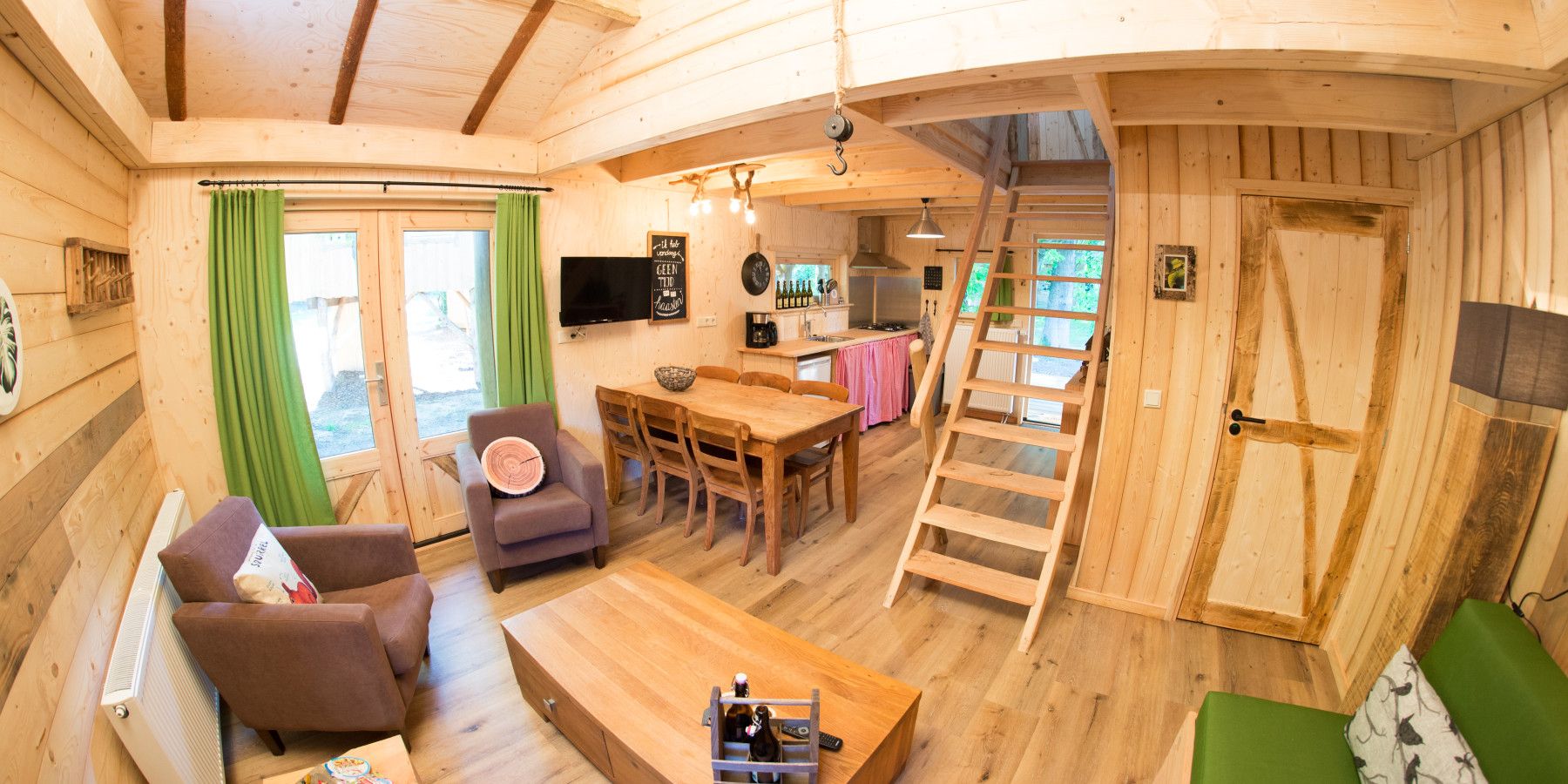 Een houten cabin met een eethoek, een bank, een televisie en een keuken.