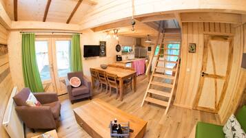 Een houten cabin met een eethoek, een bank, een televisie en een keuken.