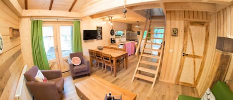 Interior de una cabaña de madera con comedor, sofá, televisor y cocina.