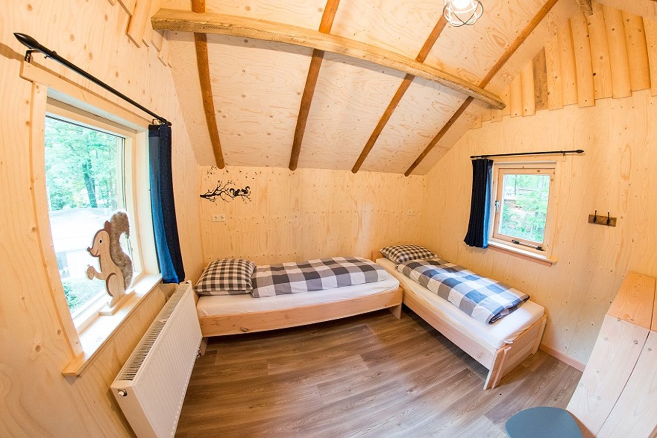 Een knus houten vakantiehuisje met twee eenpersoonsbedden, een radiator en een raam met een eekhoornbeeldje.