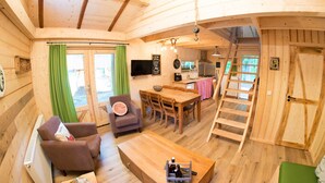 A wooden cabin interior with a dining area, a sofa, a TV, and a kitchen. - Boshuis Dora met Escapespel | Recreatiepark  d`n Mastendol (Rijen)