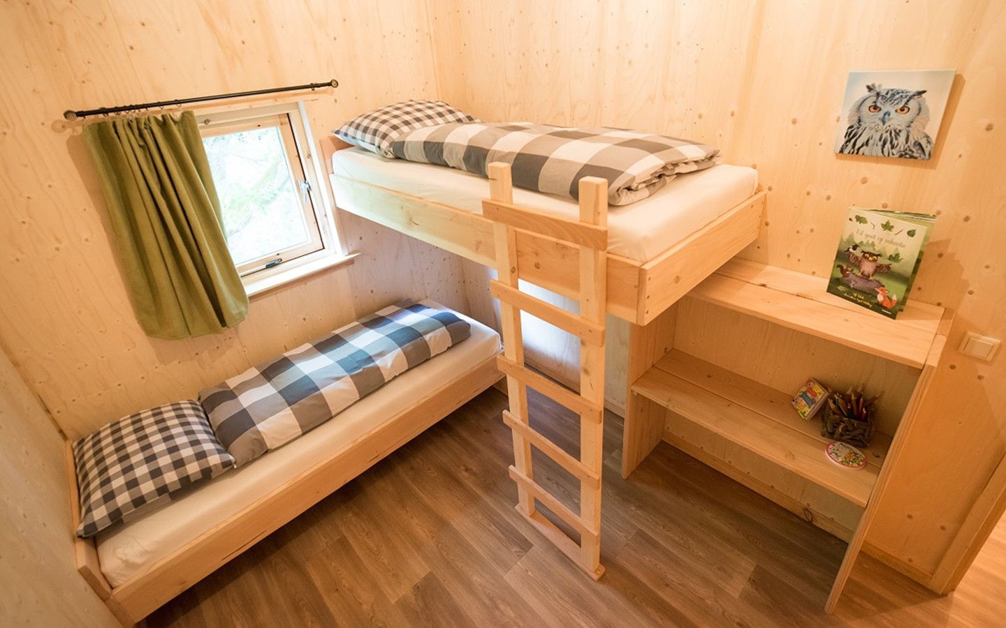 Una habitación de madera pequeña y acogedora con una cama alta, un ventanal con cortinas, una escalera y un estante con libros y una planta pequeña.
