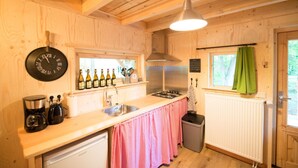 A wooden interior with a kitchen area including a sink, stove, and a clock. - Boshuis Dora met Escapespel | Recreatiepark  d`n Mastendol (Rijen)