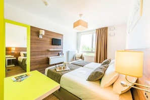 A hotel room with a bed, bedside table, lamp, TV, and a window with curtains. - Adagio Access Grenoble Université (Saint-Martin-d'Heres)