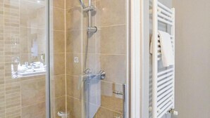 Eine Dusche mit Glasabtrennung, einer Handbrause, einem weißen Handtuchhalter und einer sichtbaren Toilette.