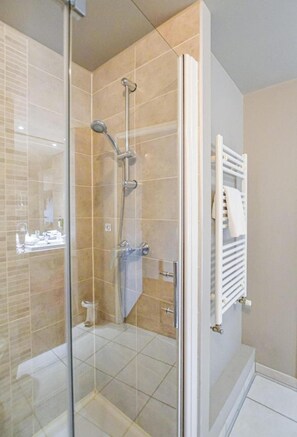 A glass-enclosed shower with a handheld showerhead, a white towel rack, and a visible toilet. - Adagio Access Grenoble Université (Saint-Martin-d'Heres)