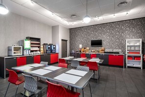 A modern cafe with tables and chairs, a coffee machine, and a TV screen.