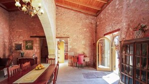 A rustic stone interior with a wooden dining table, chairs, a chandelier, and a cabinet. - Silver Gem Villa with Private Pool (Frantzeskiana Metochia)