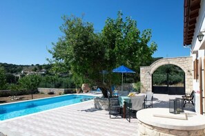 An outdoor swimming pool area with a stone archway, a table with chairs, and a blue umbrella. - Silver Gem Villa with Private Pool (Frantzeskiana Metochia)