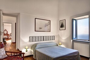 A bedroom with a bed, a nightstand, a chair, a window, and two framed pictures on the wall. - Villa Fondo Turiello – Pool & Scenic View (Massa Lubrense)