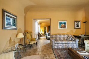 A living room with a sofa, armchair, and a coffee table. There is a door leading to another room.