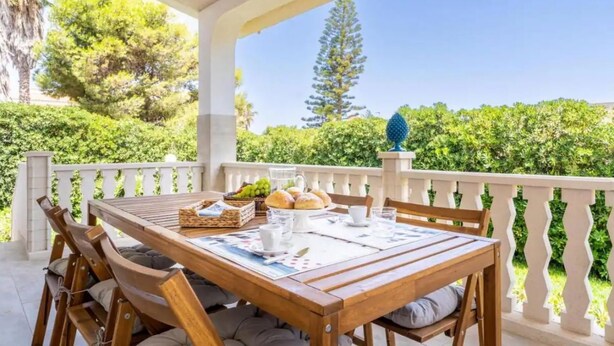 Une table en bois, dressée pour le petit-déjeuner, avec vue sur un paysage verdoyant et une balustrade blanche.
