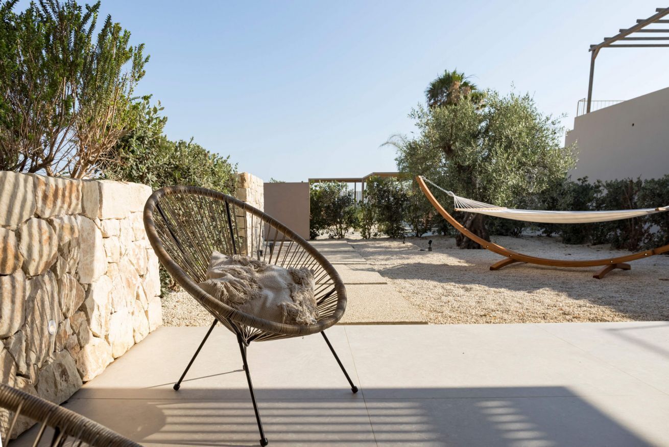 A hammock, a wicker chair, and a stone wall in an outdoor setting.
