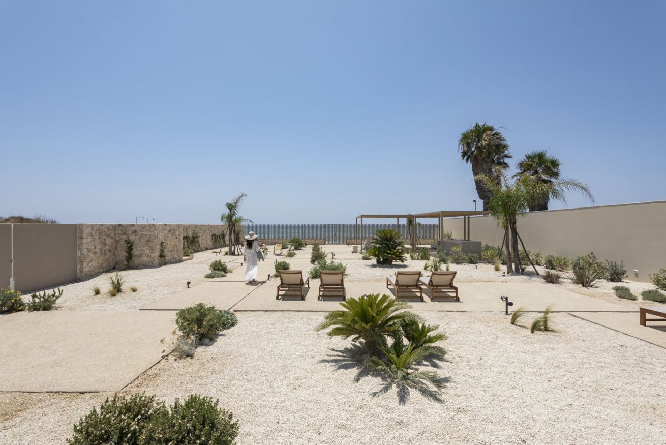 Un porxo davant la platja amb gandules, palmeres i vista al mar.