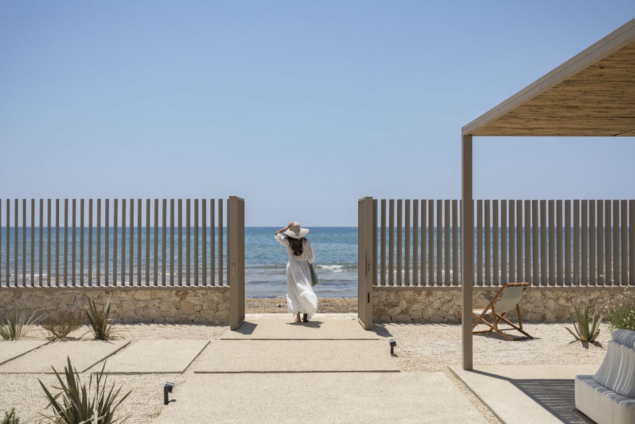 A beachside patio with a stone wall, a wooden pergola, and a beach chair.