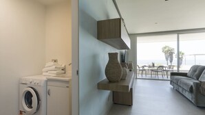 A modern apartment with a washing machine, a sofa, a dining area with a view, and a large vase on a shelf. - Cala Theresia, Alea - Sea front apartment (Pachino)