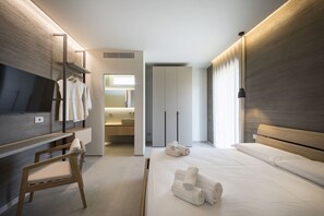 Ein modernes Hotelzimmer mit Bett, Fernseher, Schreibtisch und einem durchgehenden Türspalte sichtbaren Badezimmer.