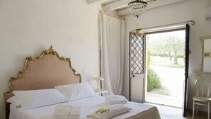 A bedroom with a large bed, a chandelier, a view through an open door, and a chair. - Casa Degli Aromi - San Lorenzo, Noto (Noto)
