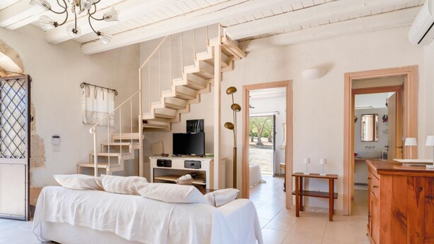 A bedroom with a bed, a TV, a staircase, a wooden cabinet, and a bathroom visible through an open door. - Casa Degli Aromi - San Lorenzo, Noto (Noto)
