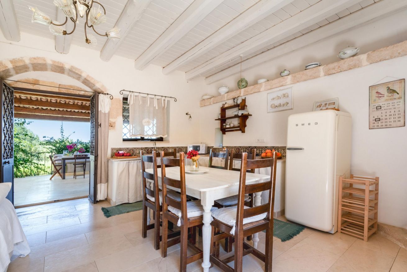 Un coin repas avec une table et des chaises, un réfrigérateur et un plan de travail de cuisine avec des étagères.
