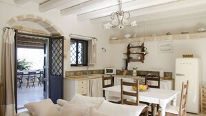 A cozy kitchen with a dining area, featuring a white table, wooden chairs, a chandelier, and a view through an open door. - Casa Degli Aromi - San Lorenzo, Noto (Noto)