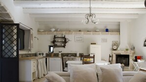 A compact living space with a kitchenette, a sofa with cushions, a dining table, and a fireplace. - Casa Degli Aromi - San Lorenzo, Noto (Noto)