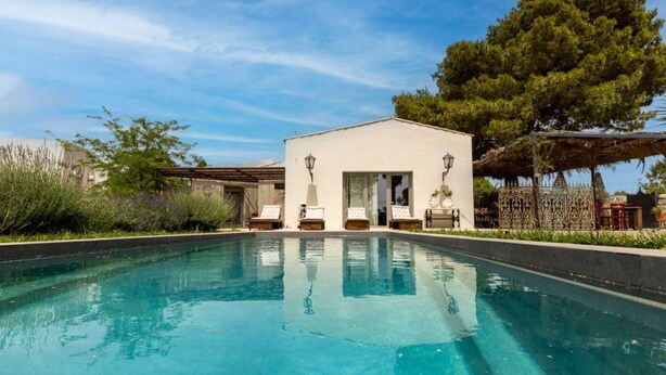 Une piscine avec un bâtiment en arrière-plan, le tout entouré de verdure.