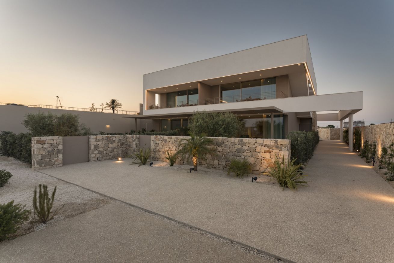 Una casa moderna de dos pisos con fachada de piedra, un espacio exterior cubierto y cielo despejado.