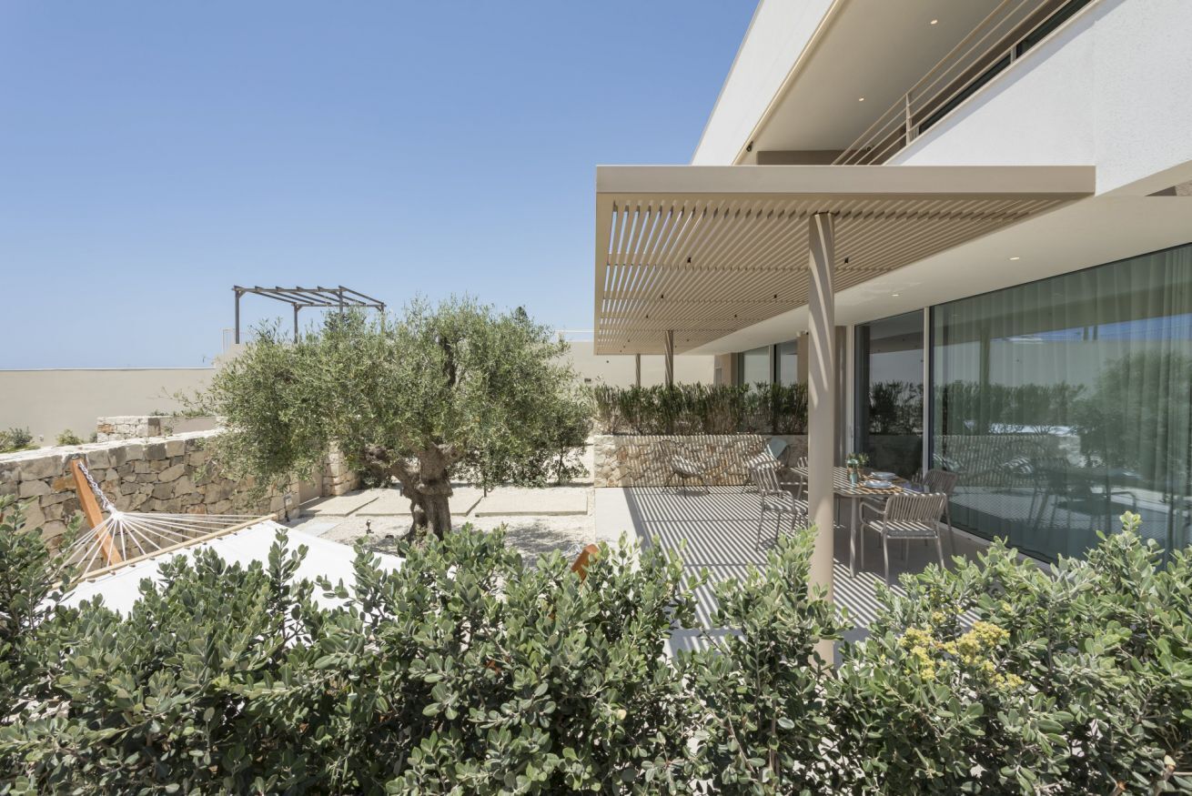 Een modern terras buiten met een hangmat, een pergola en een eethoek met tuinmeubilair.