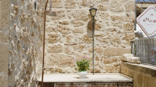 Un muro de piedra con un farol de metal, un caño de agua y un cartel con texto.