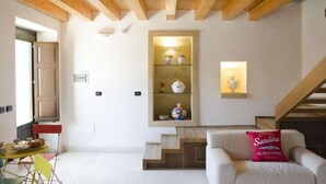 Una sala de estar con sofá, una mesa con sillas, una escalera y una estantería con adornos.