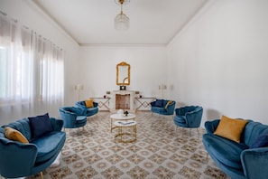 Una habitación con cuatro sillones azules, una mesa de centro blanca, un espejo y un suelo estampado.
