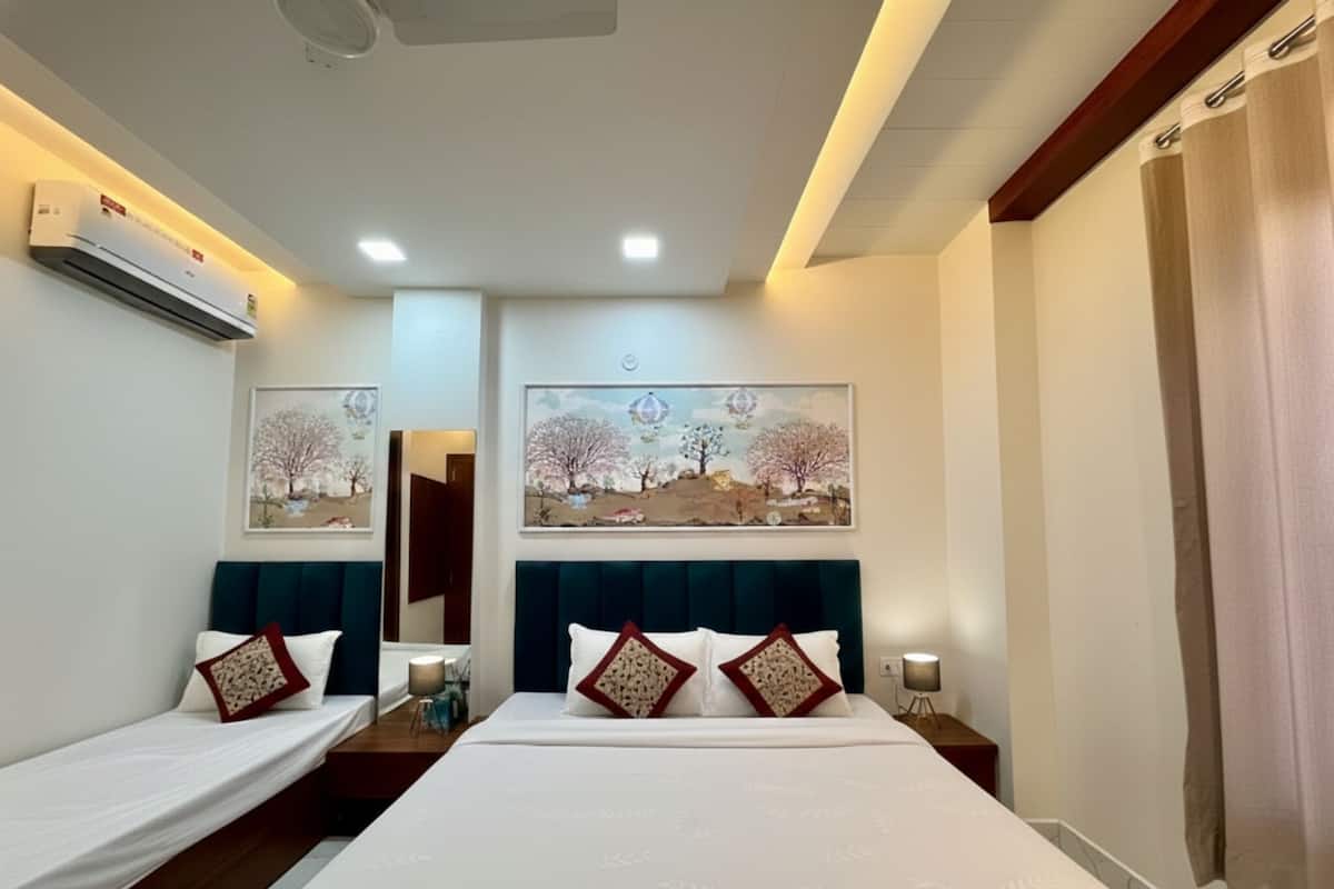 A hotel room with a large bed, two smaller beds, a ceiling fan, an air conditioning unit, and artwork on the walls.