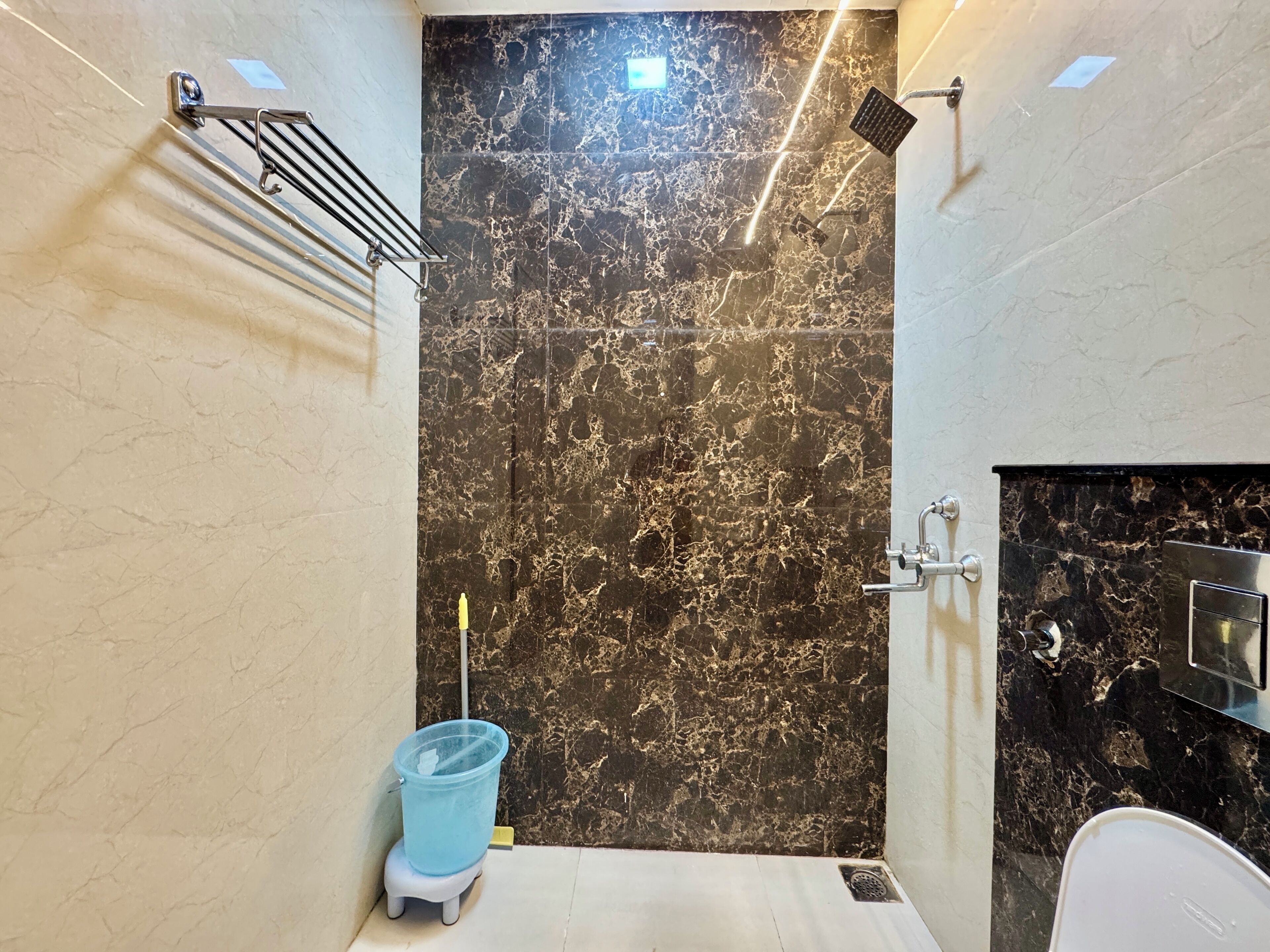 Un baño con pared de mármol, ducha, inodoro y un cubo de basura azul.
