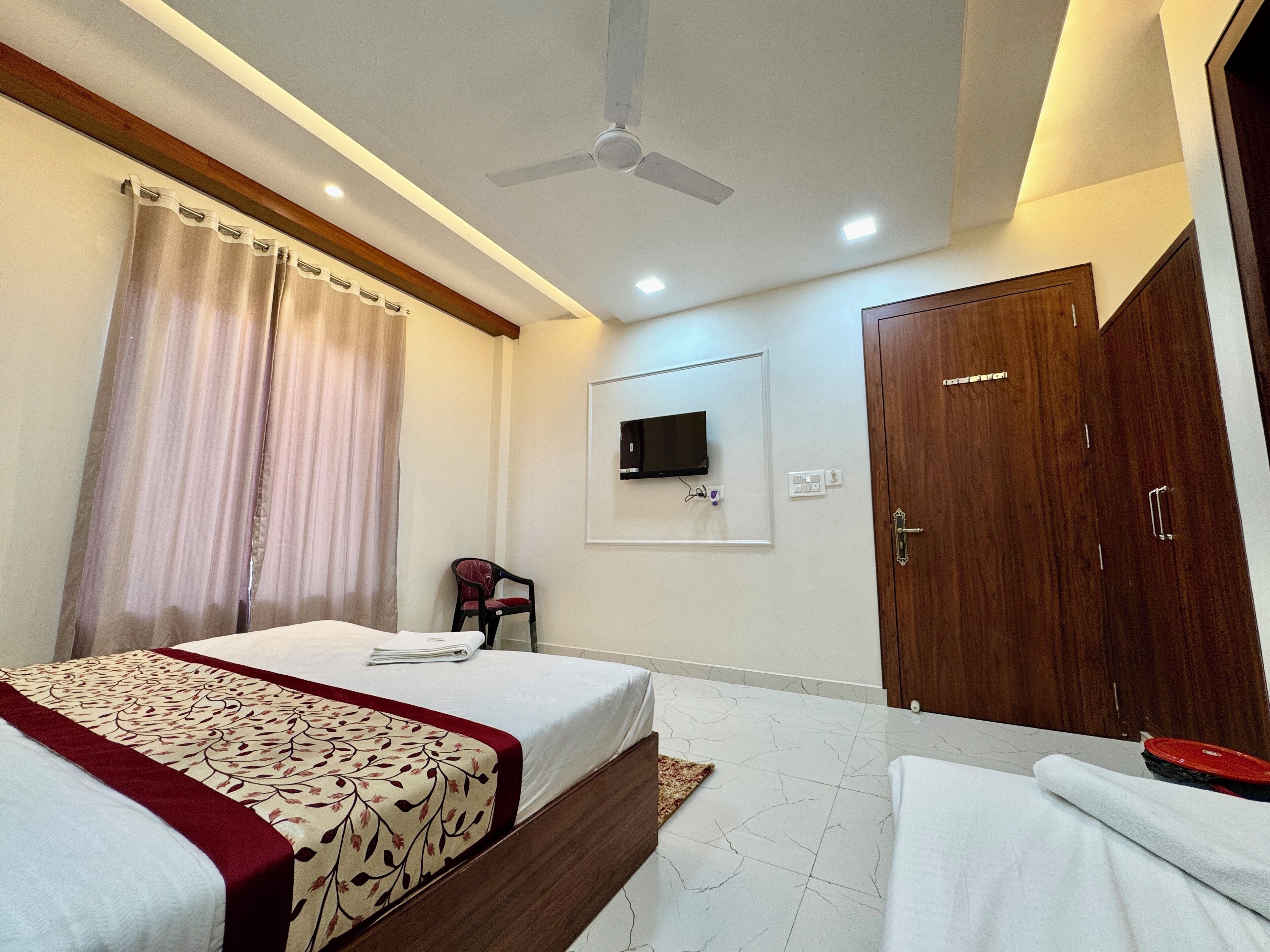 A hotel room with a bed, a wardrobe, a television mounted on the wall, and a ceiling fan.