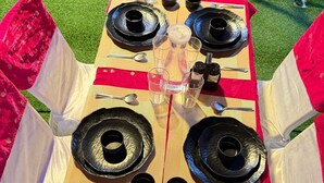 Een tafel gedekt met borden, bekers en een karaf, omringd door witte en rode gordijnen.