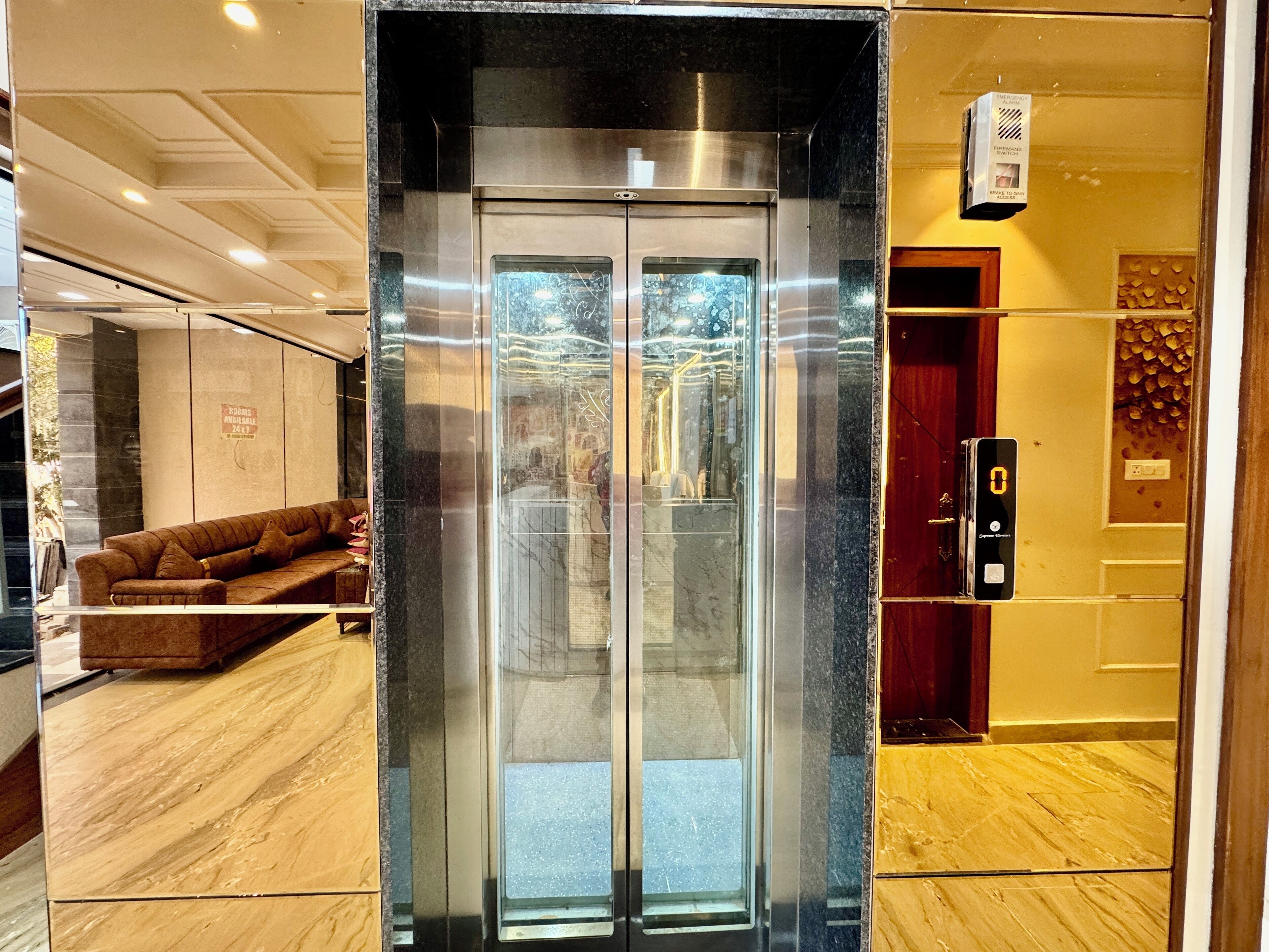 En elevator med glasdør, et receptionområde med sofa og en trægulv.