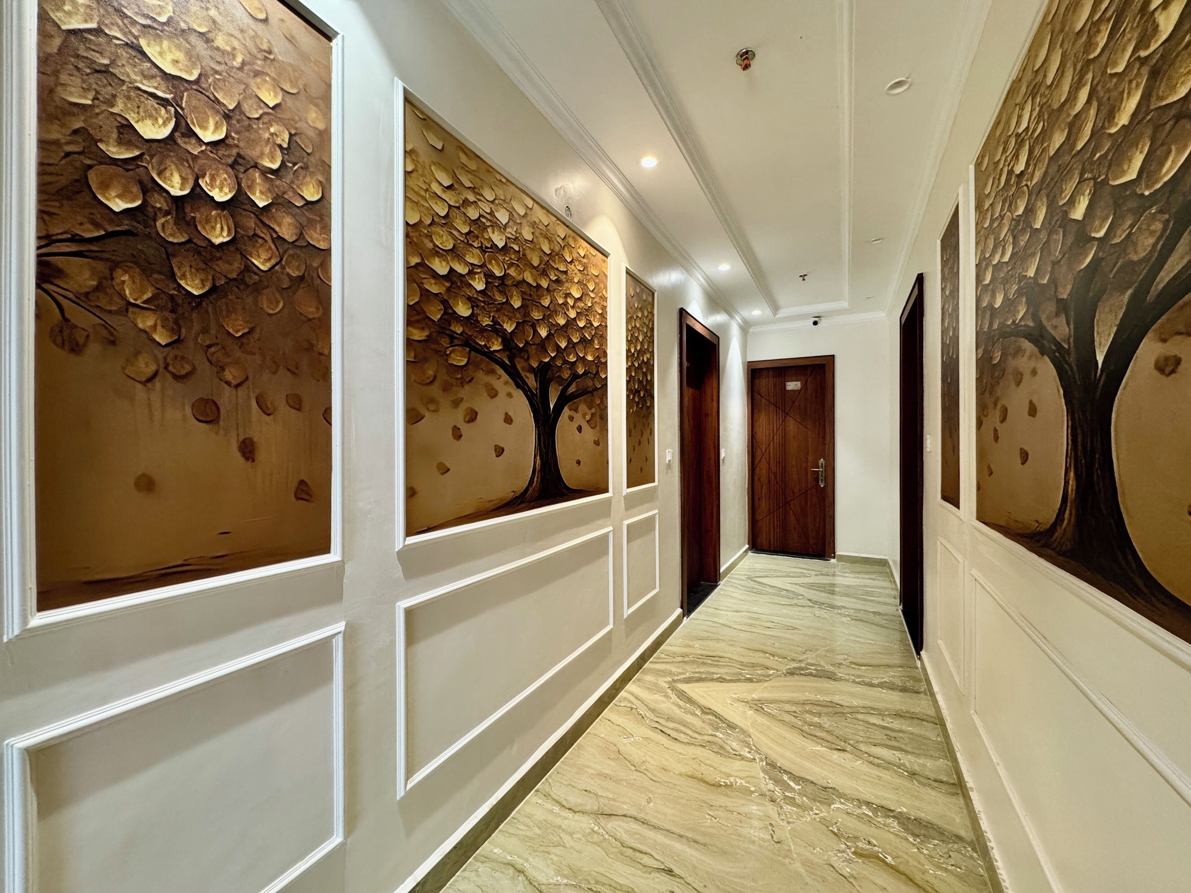 Un couloir doté d’un sol en marbre, de lambris blancs et de peintures murales représentant des arbres.