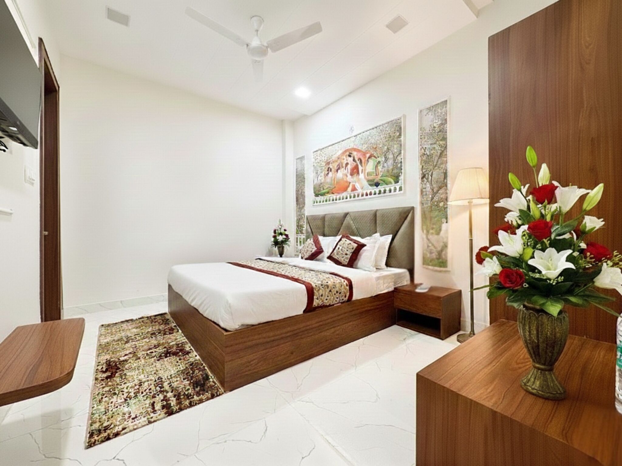 A bedroom with a bed, nightstands, a vase with flowers, a ceiling fan, and a painting on the wall.