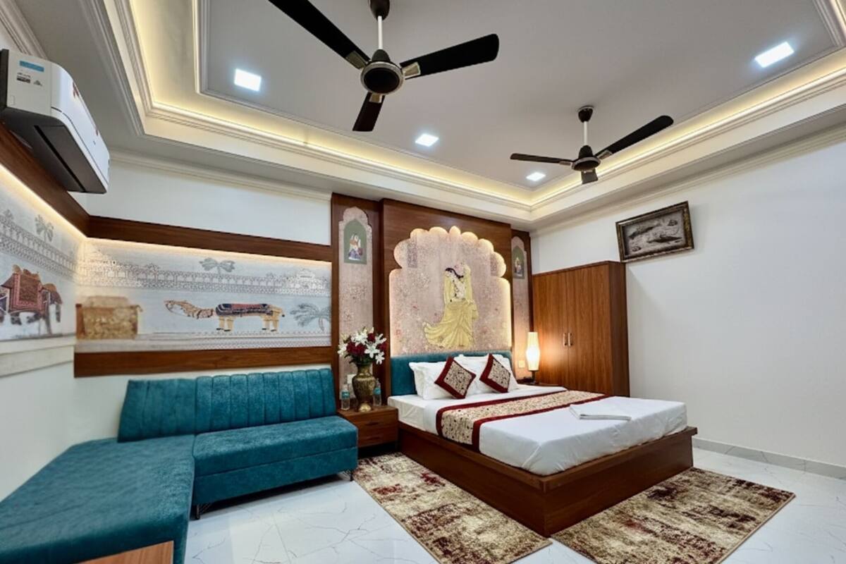 A bedroom with a bed, two ceiling fans, a nightstand, a blue sofa, decorative wall art, and a wooden wardrobe.