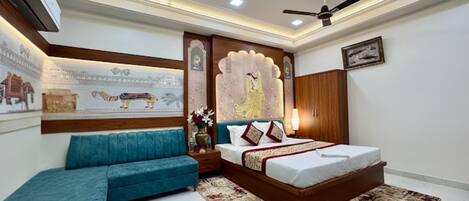 A bedroom with a bed, two ceiling fans, a nightstand, a blue sofa, decorative wall art, and a wooden wardrobe.