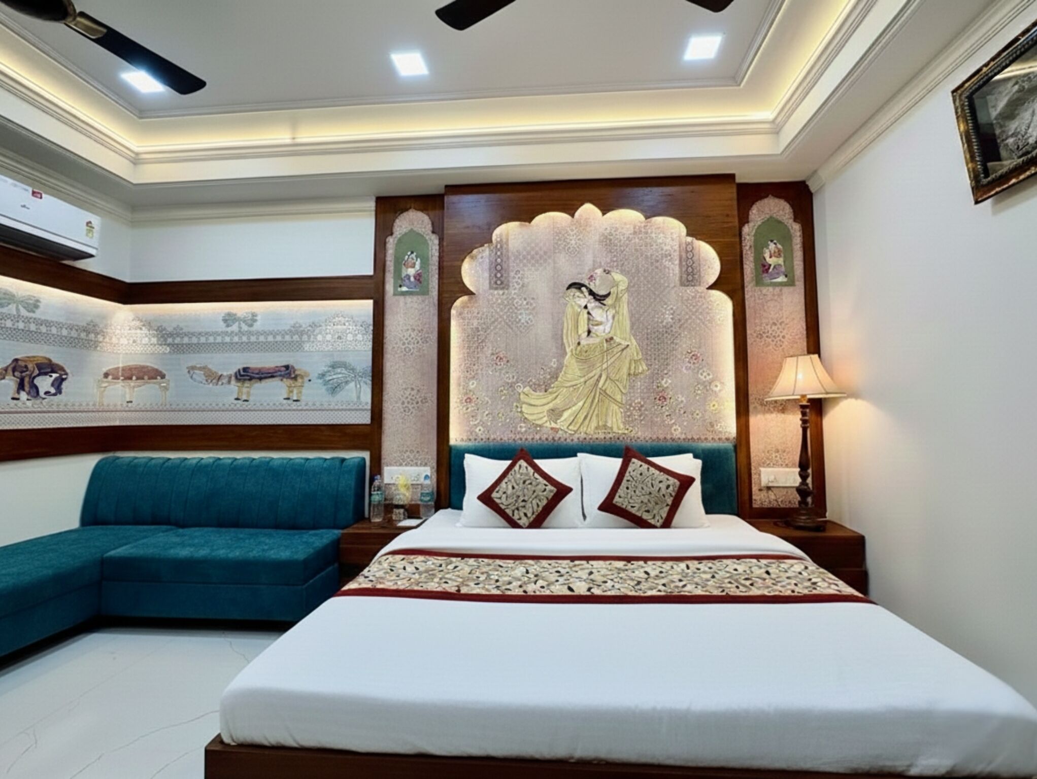 Quarto com cama, sofá azul, parede decorativa e ventoinha de teto.